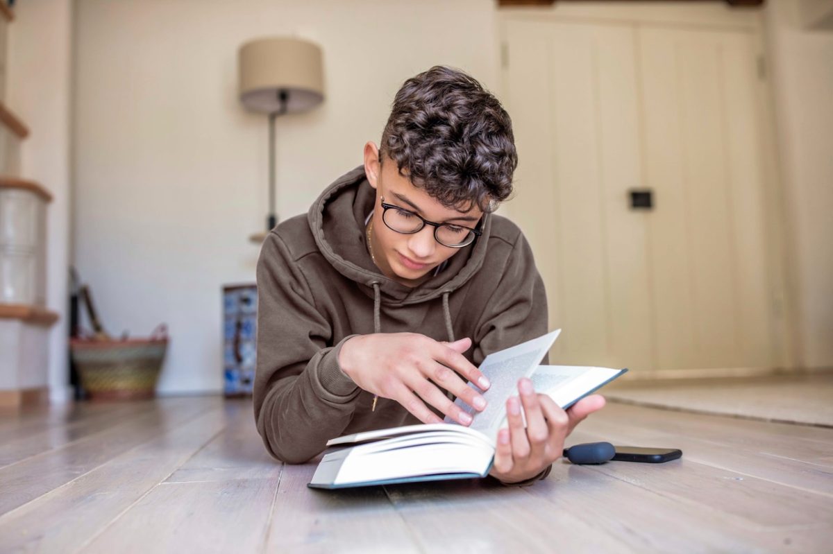 Boy lying on the floor at home reading a book
