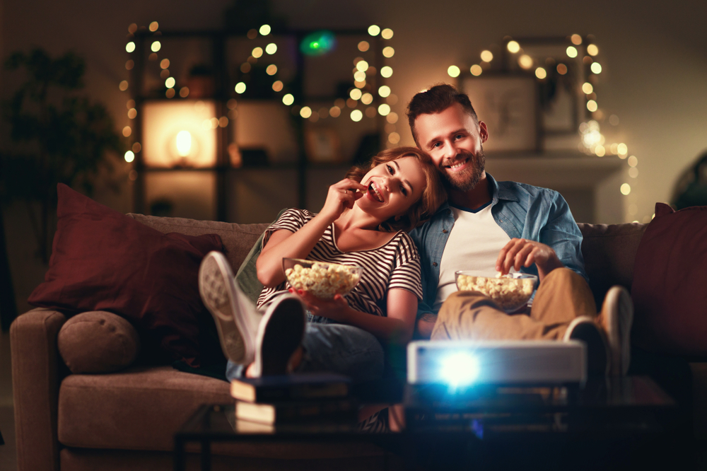 Family,Couple,Watching,Television,Projector,At,Home,On,The,Sofa