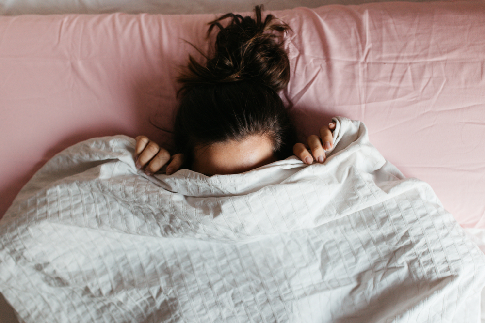 Playful,Young,Woman,Hiding,Face,Under,Blanket,While,Lying,In