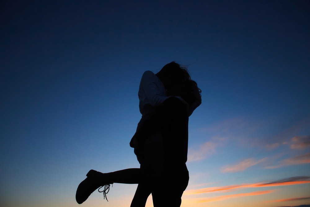 Young,Couple,Hugging,Each,Other,And,Kissing,At,Orange,Sunset.