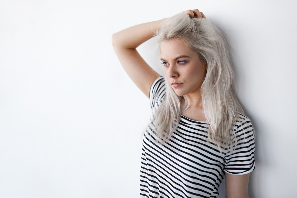 Beautiful,Young,Blond,Woman,Posing,While,Leaning,On,White,Wall