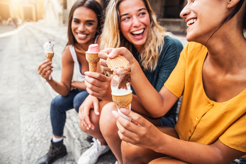 Laughing,Teenage,Girls,Eating,Ice,Cream,Cones,On,City,Street