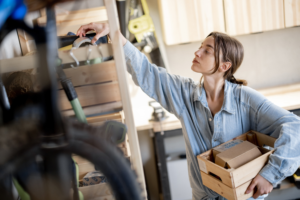 Young,Handywoman,Searching,Some,Working,Tools,On,A,Wooden,Shelves