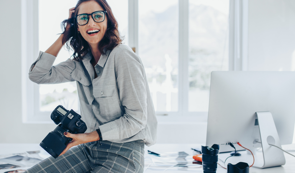 Smiling,Female,Photographer,With,A,Professional,Camera,Sitting,On,Her