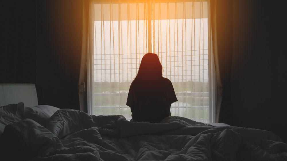 Silhouette,Of,Woman,Sitting,On,The,Bed,Beside,The,Windows