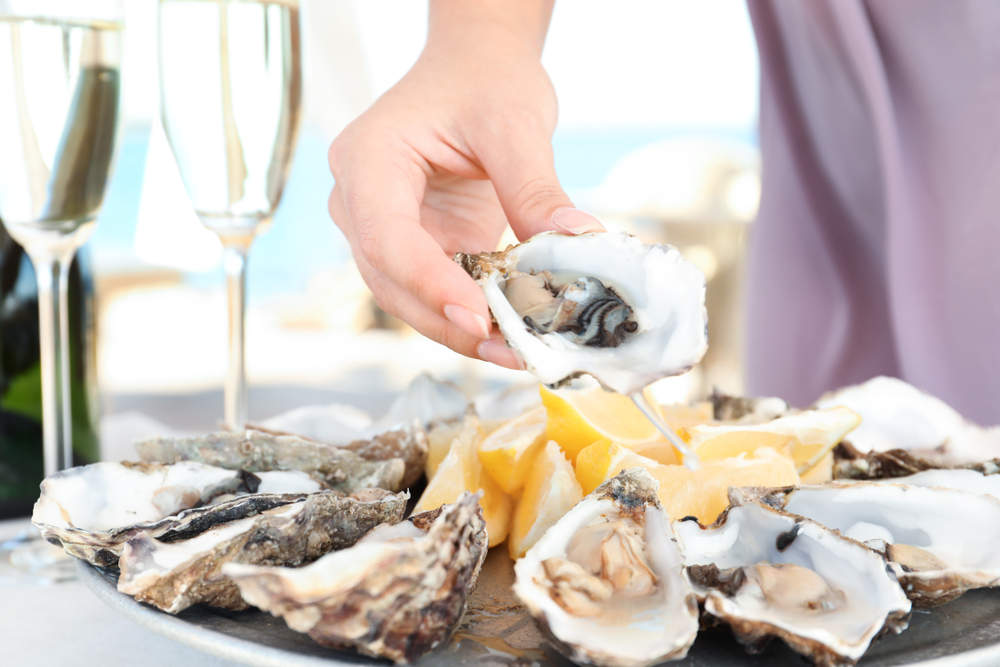 Woman,Holding,Fresh,Oyster,Over,Plate,,Focus,On,Hand