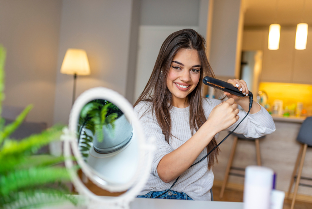 Woman,Using,A,Hair,Straightener,While,Looking,Into,The,Mirror.