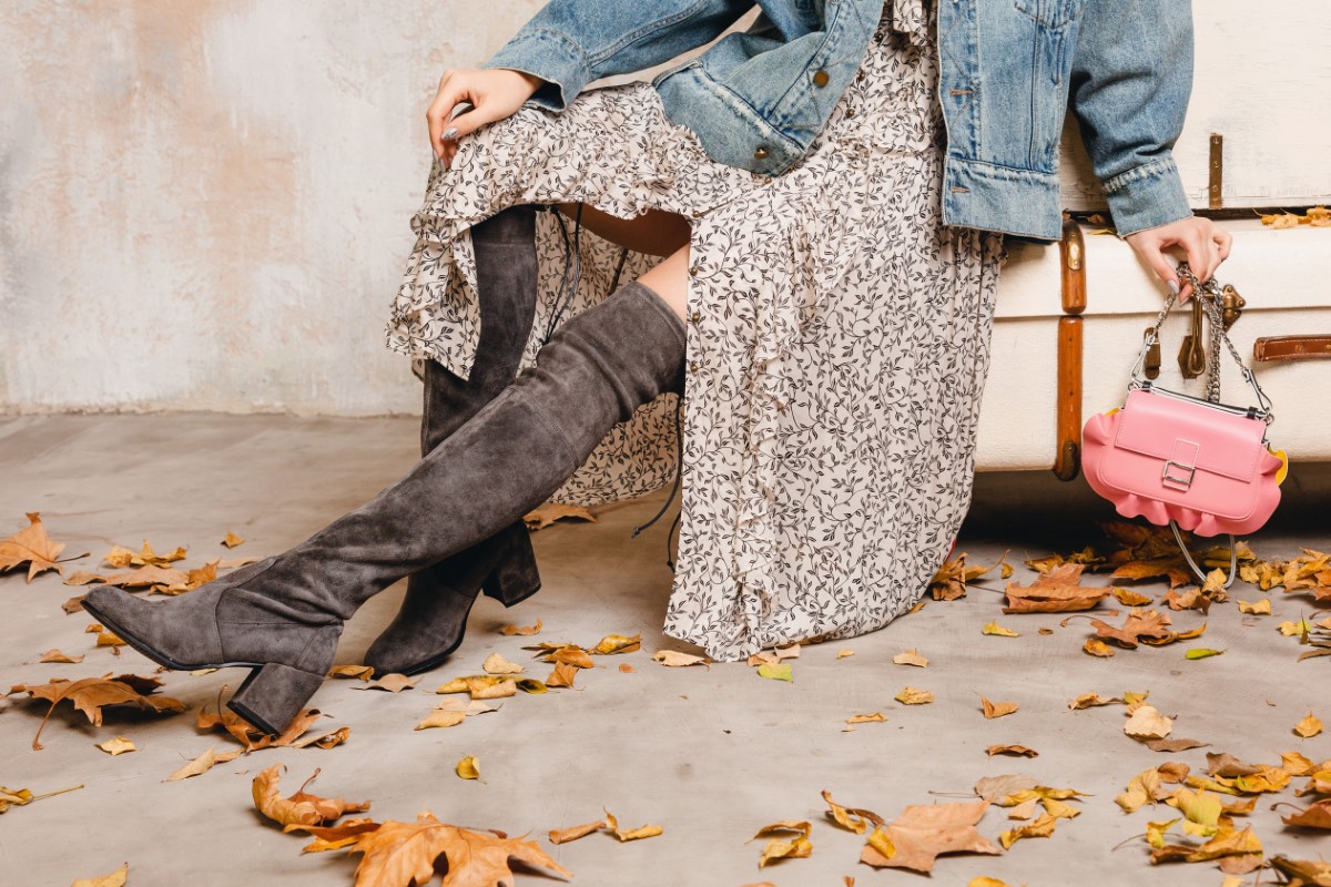attractive stylish blonde woman in jeans oversize jacket walking against wall in street, autumn leaves, fashion trend, wearing dress, high boots, purse, travel with vintage suitcases, urban style