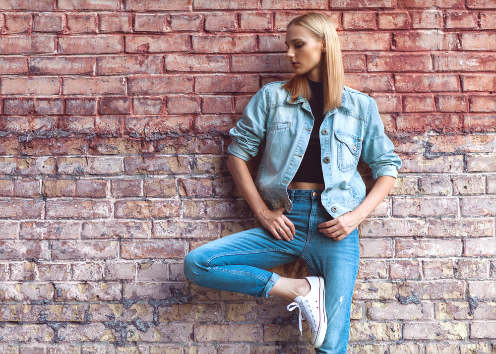Fashion,Girl,Standing,Near,Brick,Wall,In,Denim,And,Sneakers.