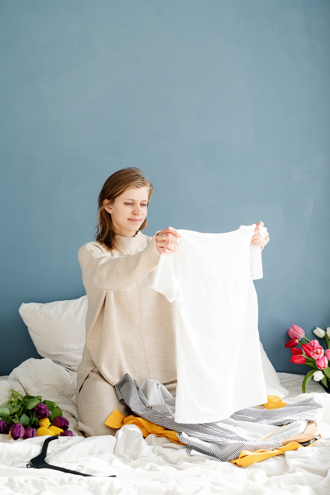 Young,Woman,Organizing,Clothes,Sitting,On,The,Bed,At,Home