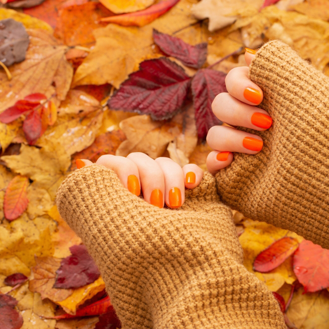 Female,Hands,With,Orange,Manicure,On,Background,Of,Autumn,Leaves