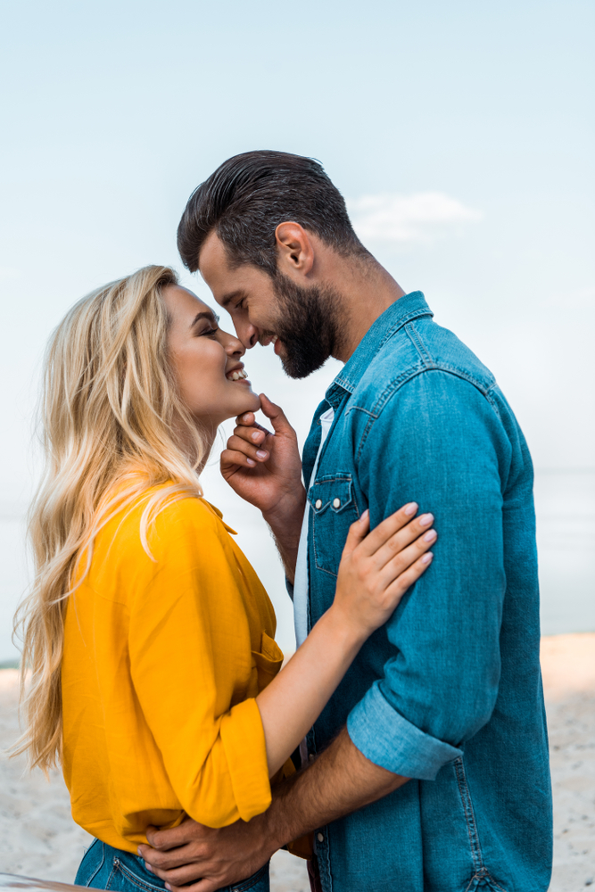 Side,View,Of,Smiling,Couple,Touching,With,Noses,On,Beach