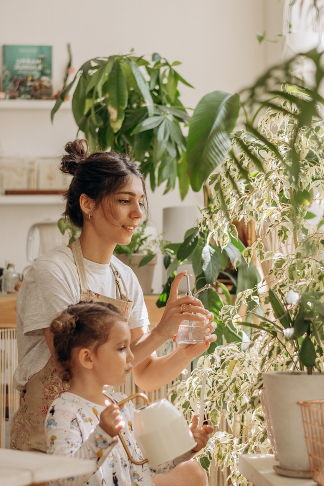 Young,Woman,With,Her,Little,Daughter,Is,Watering,Houseplants,At
