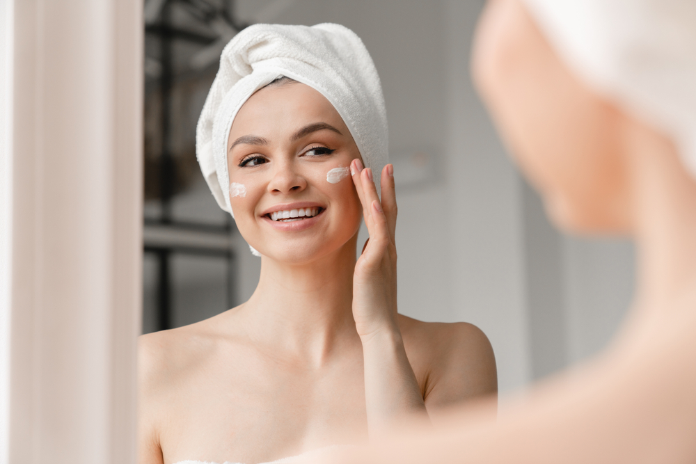 Young,Caucasian,Woman,In,Bath,Towel,Applying,Face,Body,Cream