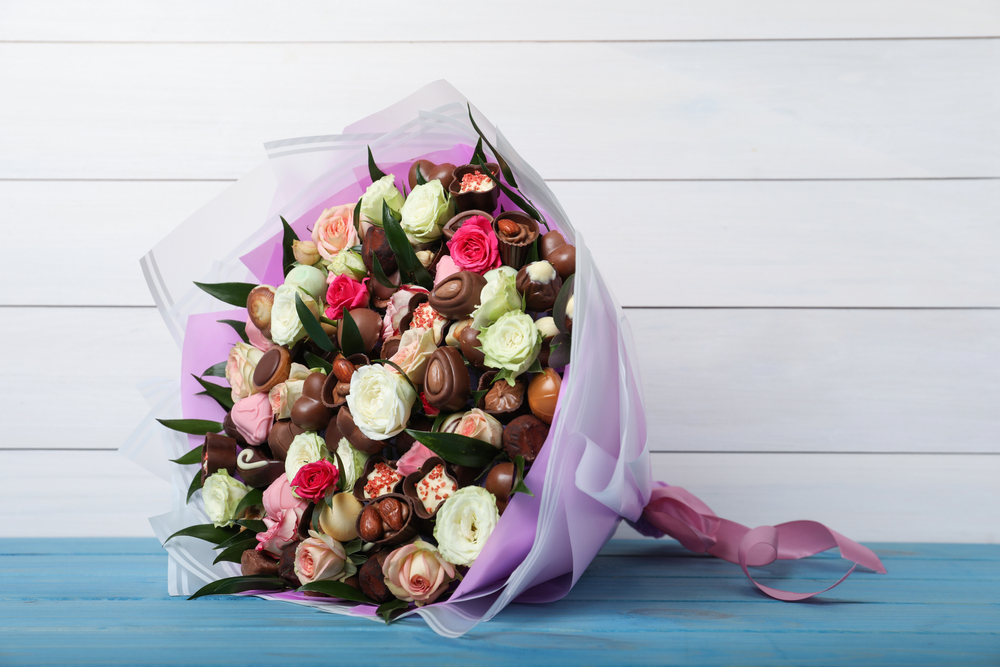 Beautiful,Bouquet,Of,Flowers,And,Chocolate,Candies,On,Light,Blue