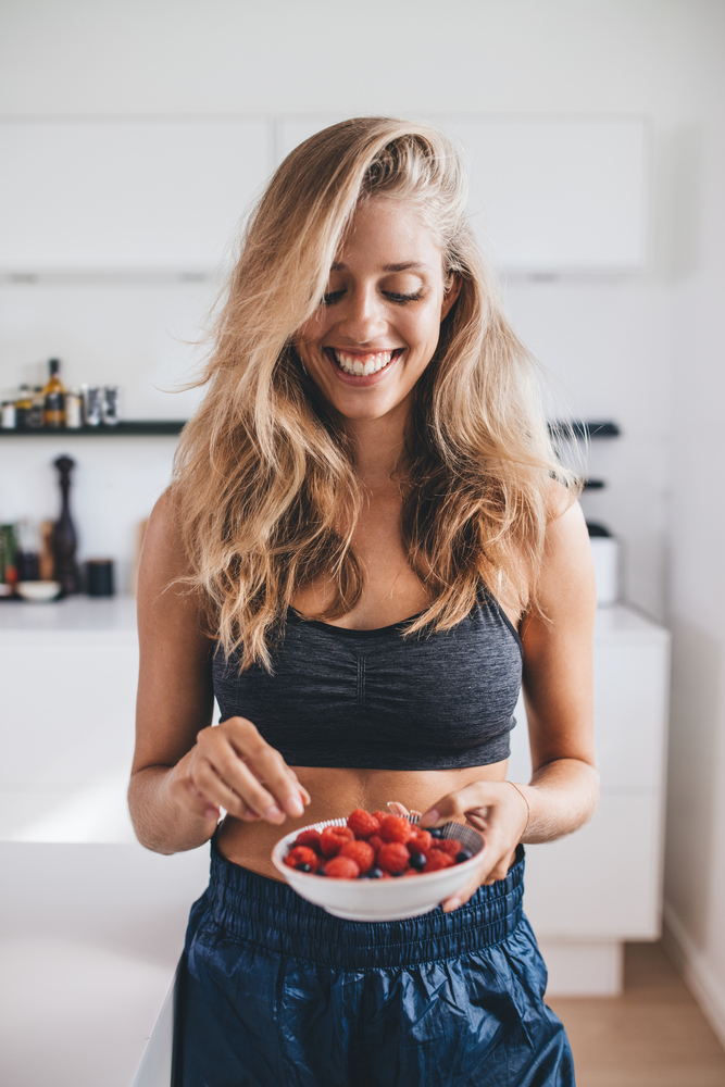 Healthy,Young,Woman,In,Kitchen,Holding,A,Bowl,Of,Berries.