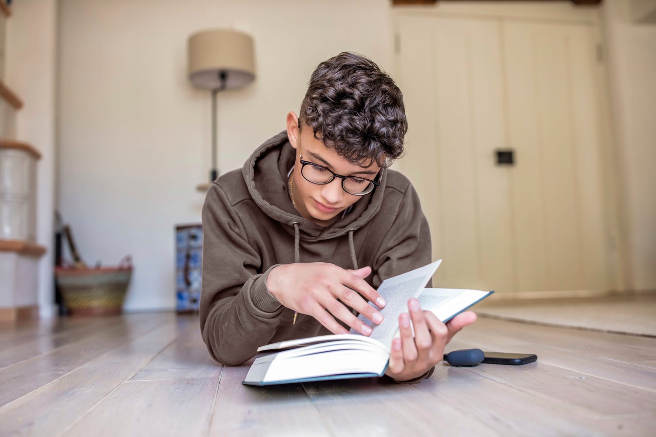Boy lying on the floor at home reading a book